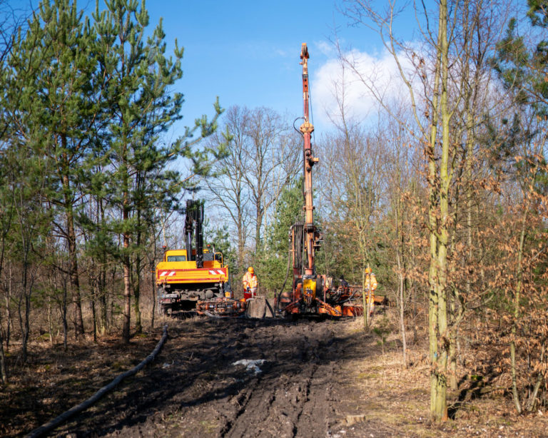 Bohrgerät und kleiner LKW mit Kranarm auf einem Waldweg