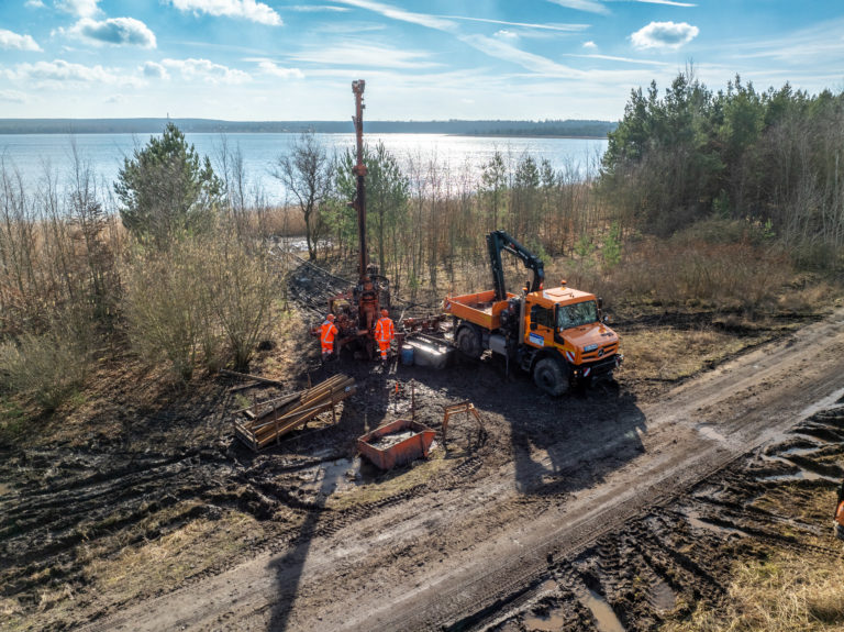 Bohrgerät und kleiner LKW mit Kranarm am Ufer bei der Arbeit